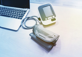 Electronic Blood Pressure Monitor or Sphygmomanometer and laptop on the wooden table background. Healthcare concept.