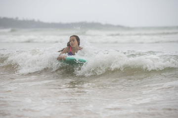  Female child surfing the waves on a boogie board coming  towards the camera on the beach  on a bright tropical summer holiday 