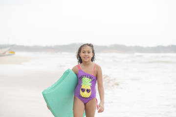 Mixed-race female child walking towards the camera on the beach and waves on a bright tropical...