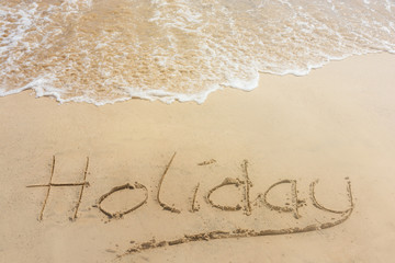 Fototapeta na wymiar The word holiday written in the sand at the beach