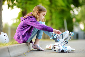 Pretty little girl learning to roller skate on summer day in a park. Child wearing safety helmet...