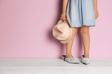Little girl in oversized shoes near color wall with space for text, closeup on legs