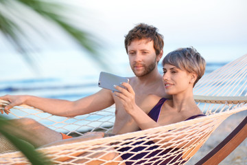 Young couple taking selfie in hammock on beach