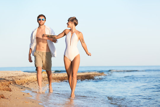 Happy young couple walking together on beach. Space for text