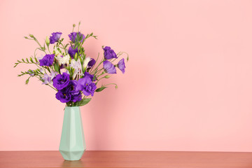 Beautiful bouquet of eustoma and freesia flowers in vase on color background. Space for text