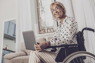 Watching movie. Blonde-haired elderly woman feeling relieved while watching comedy movie sitting in...