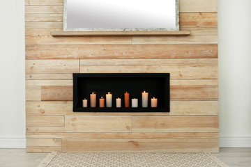 Burning candles on shelf in wooden wall indoors