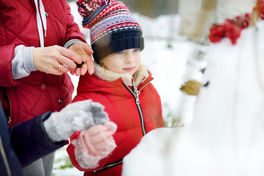 Cute Little Girl And Her Grandma Building A Snowman In The Backyard