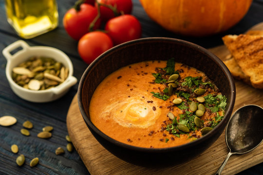 Pumpkin soup with sour cream and pumpkin seeds on a wooden table.