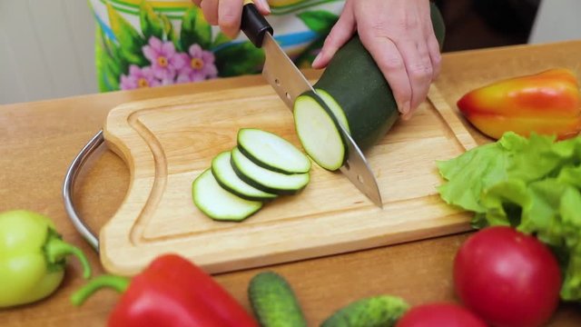 Women's hands Housewives cut with a knife fresh zucchini on the cutting Board of the kitchen table