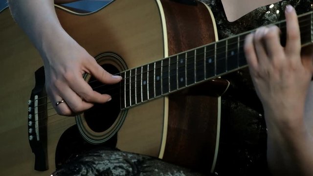 Focus on fingers fingering the strings. Close-up of the hands of a girl playing an acoustic guitar.