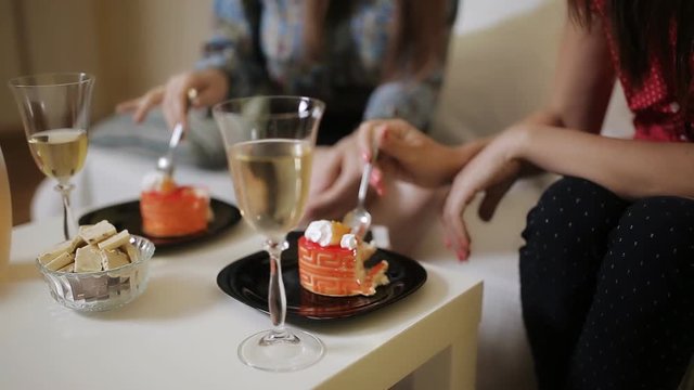 Two women talk, drink wine and eat cake at home on the couch