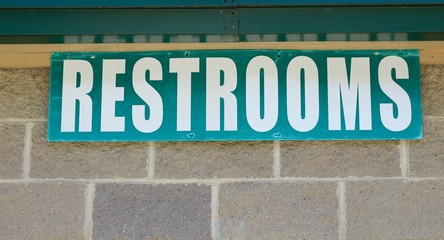 A green restrooms sign on the concrete cement wall.