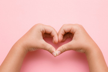 Heart shape created from little girl's hands on the pink background. Love, happiness and safety concept. Empty place for text.