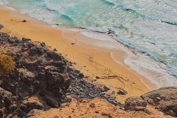 Fototapeta na wymiar Beautiful cliff landscape with rocks and turquoise sea with waves and people sunbathing in Fuerteventura, Canary Islands, Spain