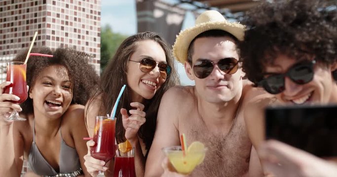 Guy filming a video of his friends in swimming pool drinking cocktails and chatting. always online 4k