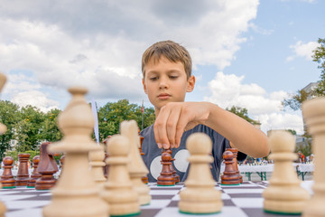 Kid playing chess at chessboard outdoors. Boy thinking hard on chess combinations