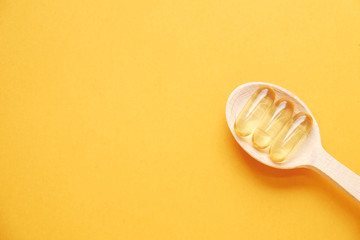 Three omega 3 fish liver oil capsules in wooden spoon. Big golden translucent pills on yellow...