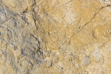 The texture of the stone wall of the rock with multi-colored shades, cracks, chips, scratches and small stones.
