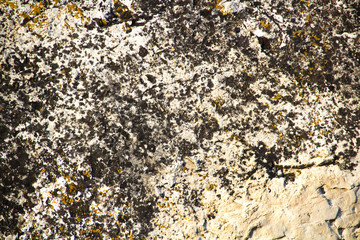 The texture of the stone wall of the rock with multi-colored shades, cracks, chips, scratches and small stones.