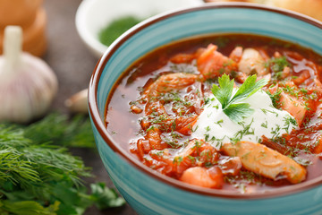 National russian red soup borscht with sour-cream and parsley in blue bowl.