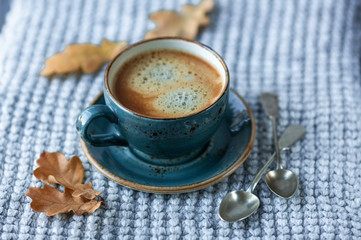 Blue cup whith coffee, knitted sweater, autumn leaves on wooden background. Cozy morning.