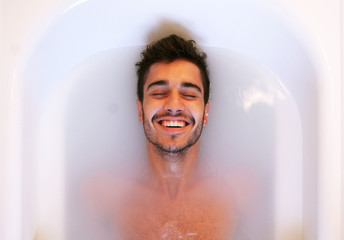 Portrait of a young spanish man smilling in a white bath tub
