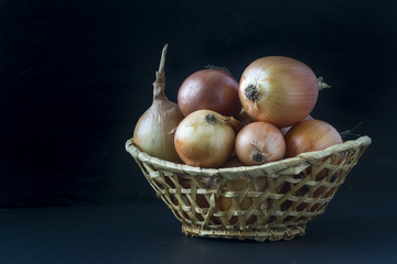 Raw onion in a basket on a black background.