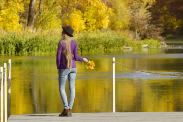 Fototapeta na wymiar Girl in hat standing on the dock. Autumn sunny day. Back view