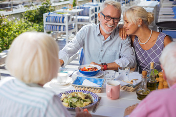 Pleasurable time. Delighted joyful people sitting around the table while enjoying their time together