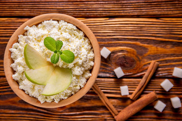 homemade cottage cheese in a wooden bowl, mint and sugar cubes, cinnamon, apples lie on a wooden table