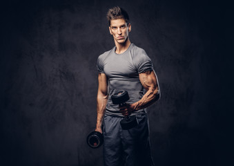 Fototapeta na wymiar Handsome sportsman with stylish hair dressed in a sportswear doing the exercises with dumbbells.