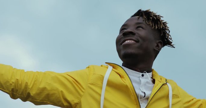African man in yellow jacket enjoy weather overcast cloudy sky with raised hands
