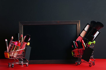 Different makeup cosmetics in shopping carts with wooden frame