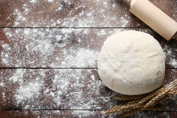 Raw dough with rolling pin and wheat ears on brown wooden table