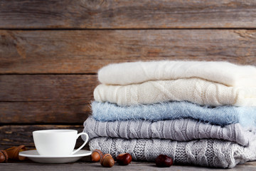 Stack of knitted sweaters with cup of tea, acorns and chestnuts