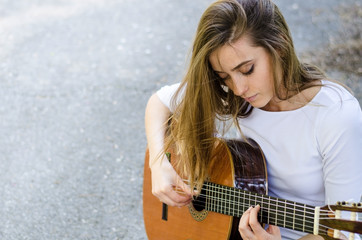 Young girl with long hair playing acoustic guitar outdoors. Copy space.