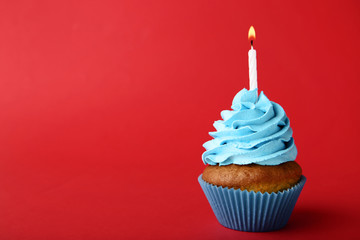Tasty cupcake with candle on red background