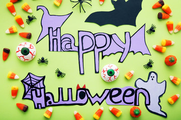 Inscription Happy Halloween with candies and paper decorations on green background