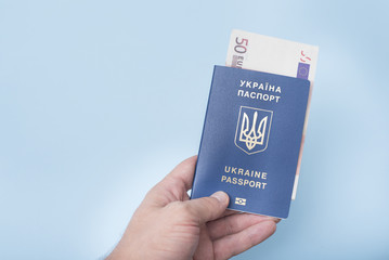 Ukrainian passport and euro cash in the man's hand. Travel concept. Blue background