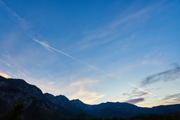 Airplane flying in the blue sky among clouds, sunlight and mountains at sunset. Austria, Salzkammergut. Austrian Alps.