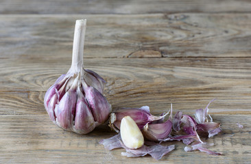 Garlic and a few cloves of garlic on a wooden kitchen table. One clove is cleaned.