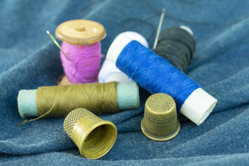 copper old thimbles, colorful threads and needles on blue fabric, close-up