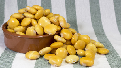 Earthenware bowl full to the brim with salted lupin beans, on top of a stripped gray cloth towel.
