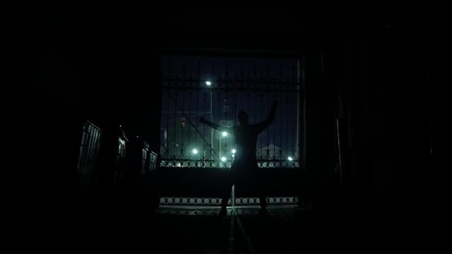 Dancing silhouette of man at dark gateway with night city lights slow-mo