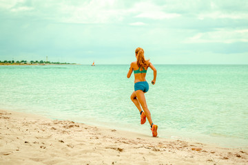 Fototapeta na wymiar Beautiful sportive woman running along beautiful sandy beach, healthy lifestyle, enjoying active summer vacation near the sea