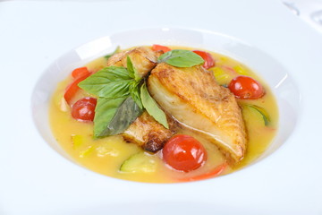 fried fish in sauce with cherry tomatoes and basil on white background