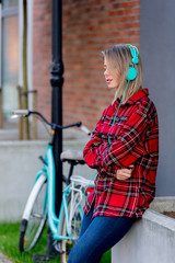 Fototapeta na wymiar Young blond girl with headphones and bicycle at urban outdoor
