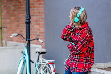 Young blond girl with headphones and bicycle at urban outdoor