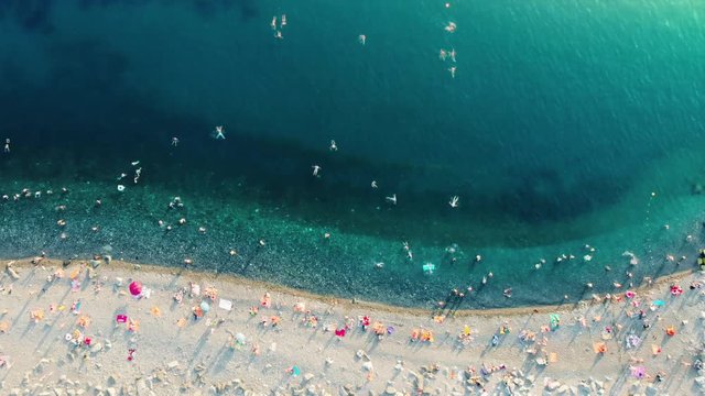 Picturesque aerial timelapse of beach life in Sochi view from above. Beautiful green and blue sea waves roll ashore, people swim in the water and sunbathe on the shore crammed with colorful umbrellas.